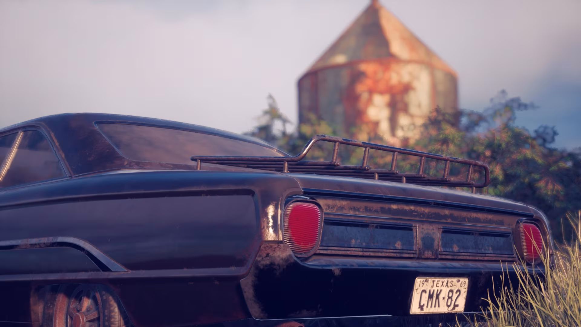 Captura de tela do jogo The Texas Chain Saw Massacre, Vista traseira de um carro antigo, escuro e enferrujado, com uma placa de Texas de 1969, número CMK-82, exibindo um porta-bagagens no teto, e um celeiro enferrujado à distância.